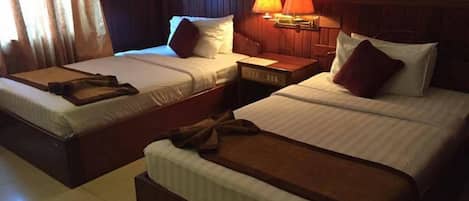 A hotel room with two single beds, a nightstand, and a lamp between the beds.