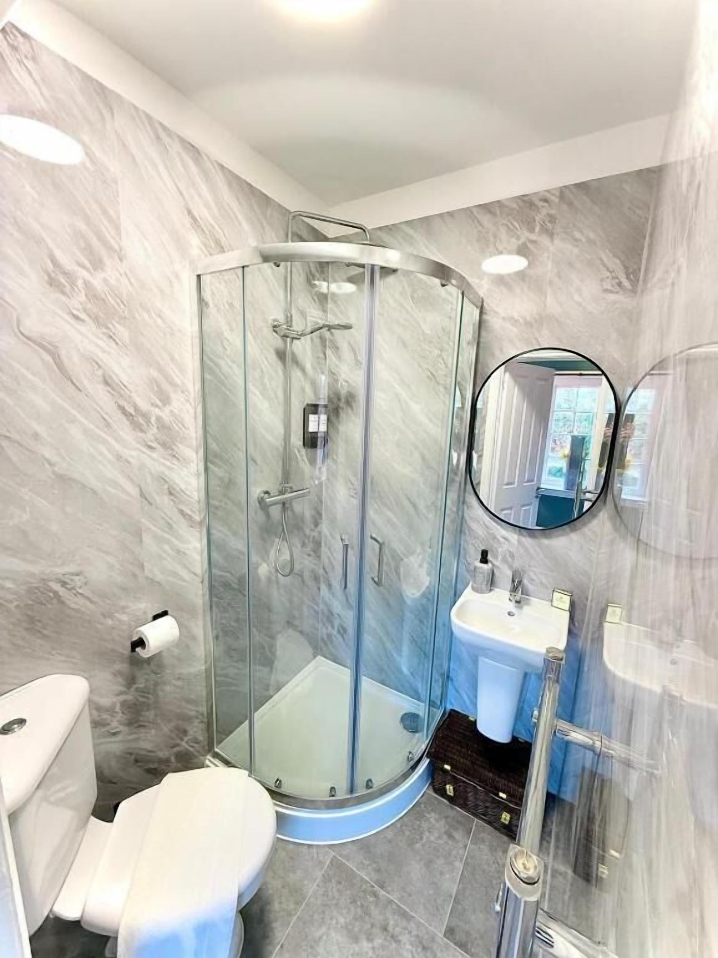 Ein modernes Badezimmer mit einer Duschkabine, einer Toilette, einem Waschbecken und einem Spiegel.