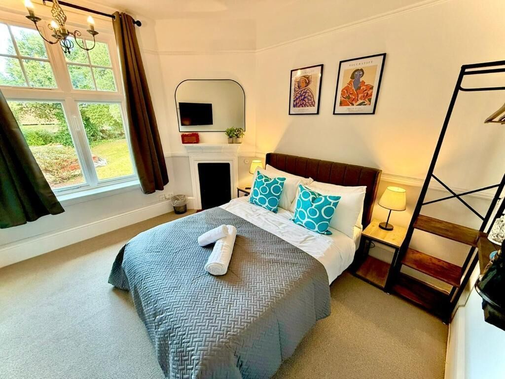 A hotel room with a bed, a fireplace, a window with curtains, and artwork on the wall.