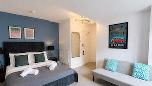 A bedroom with a bed, a sofa, a door, and a wall with a picture. - The Bay Apart-Hotel (Southwold)