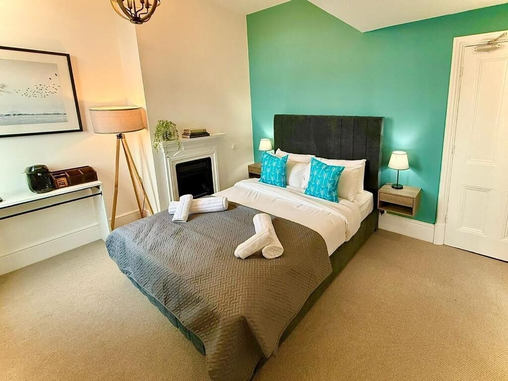 A hotel room with a bed, a fireplace, a desk, and a door.