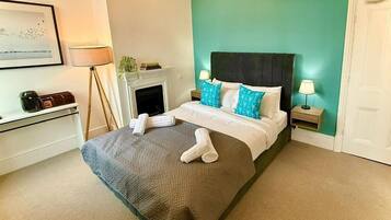 A hotel room with a bed, a fireplace, a desk, and a door.