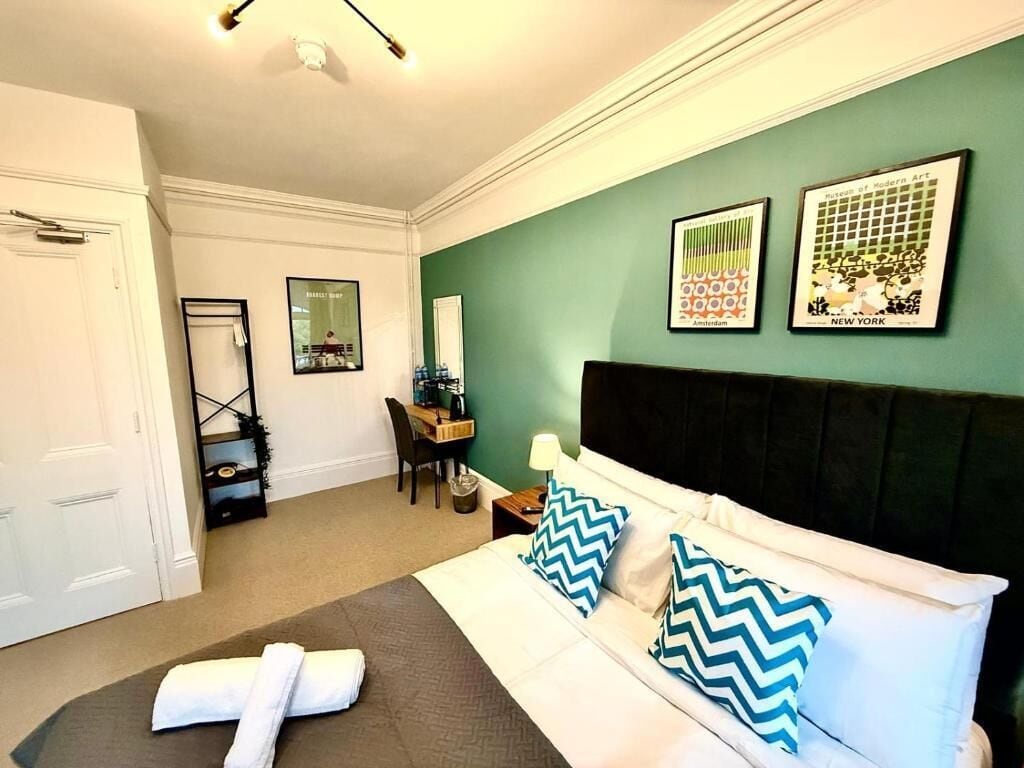 A hotel room with a bed, a desk, a chair, and artwork on the walls.