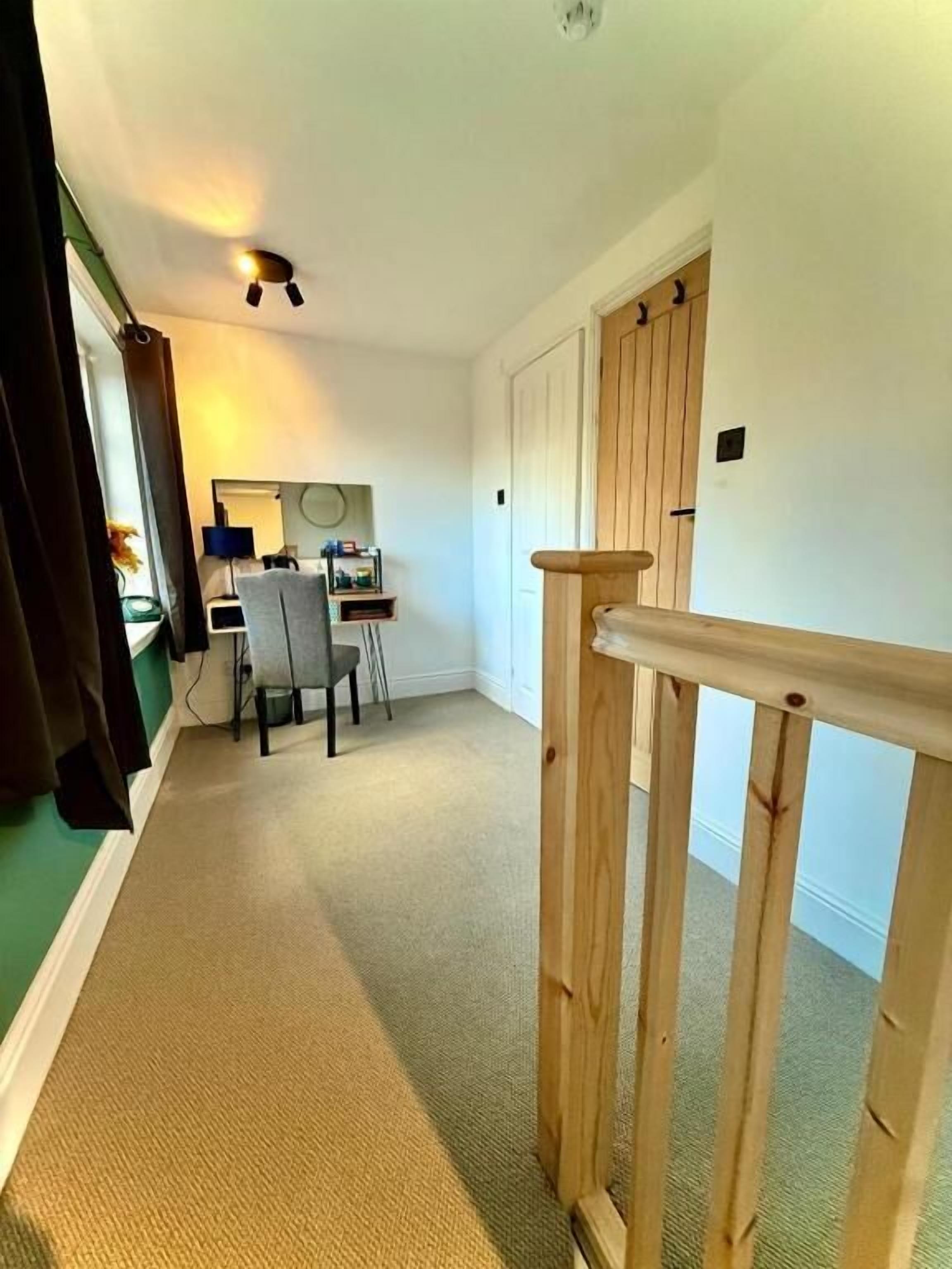 Un couloir avec une rambarde en bois, un bureau avec une chaise et une porte au fond.