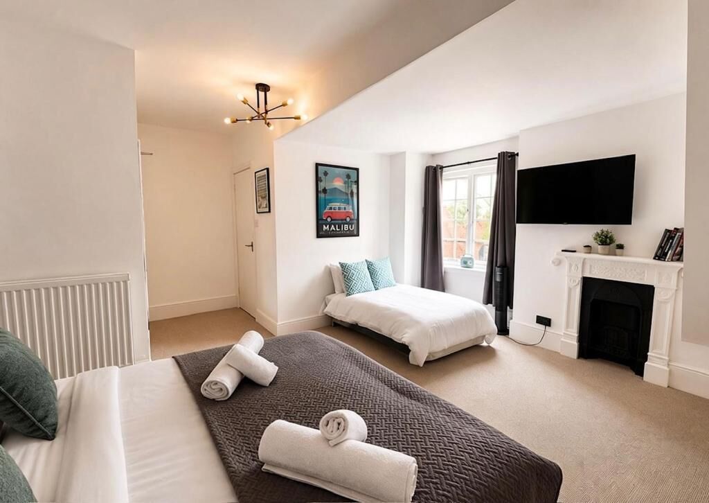 A hotel room with two beds, a flat-screen TV, a fireplace, and a poster on the wall.