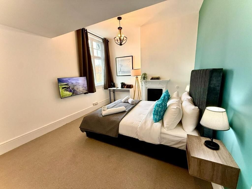 A bedroom with a bed, bedside table, lamp, and a painting on the wall.
