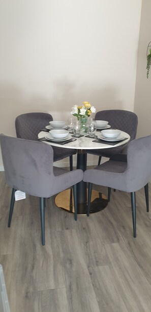 A round dining table with four chairs, a vase with flowers, and clear glassware. - Modern 2 Bedroom Apartment /Mancehster city Centre/ Sleeps 5. (Manchester)