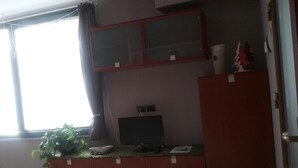 Una habitación con escritorio, computadora, ventana con cortinas y una planta pequeña.