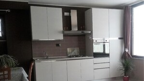 A modern kitchen with white cabinets, a built-in oven, and a window with curtains.