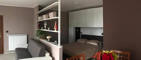 Un dormitorio con cama, mesita de noche, cómoda, estante con adornos y un radiador.