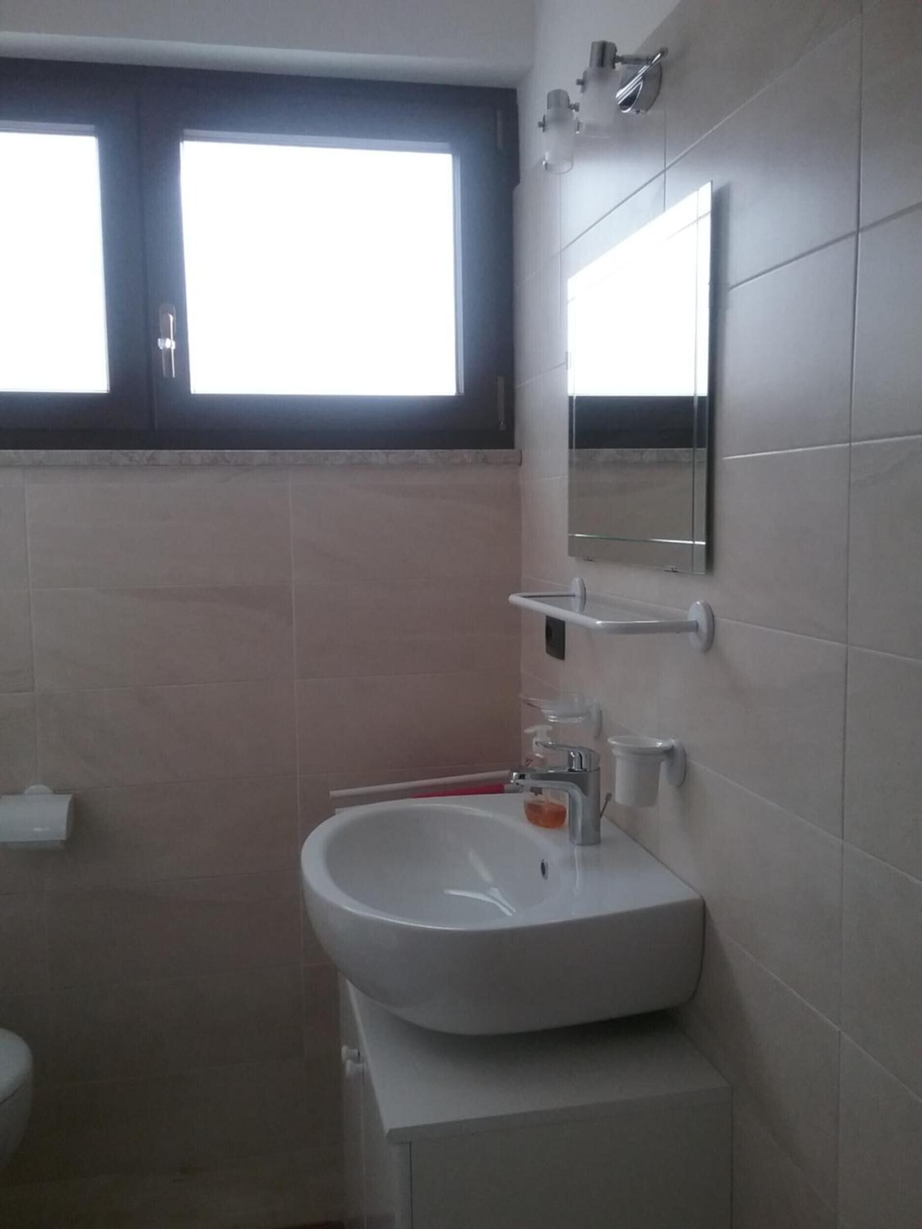A bathroom with a white sink, a mirror, and a window above the sink.