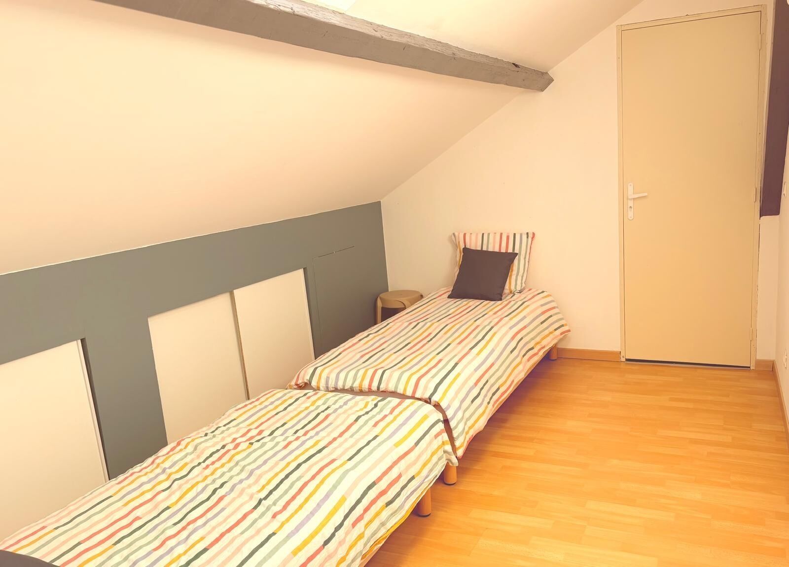 A small, single-room accommodation with two single beds, a wooden floor, and a door.