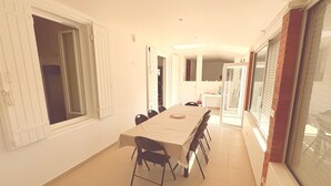 Et spiseområde med et bord og stole, et køkken i baggrunden og en skydedør.