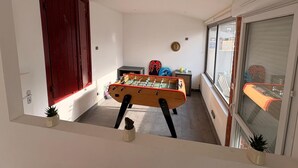 Et smalt rum med et bordtennisbord, en rød dør og et vindue med udsigt til gaden.