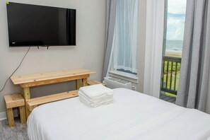 Habitació d'hotel amb un llit, un escriptori de fusta, una televisió penjada a la paret i una finestra amb vista al mar.