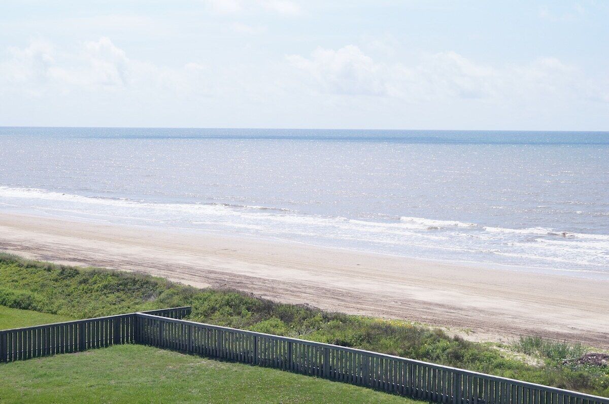 A coastal view with a sandy beach and a wooden fence in the foreground.