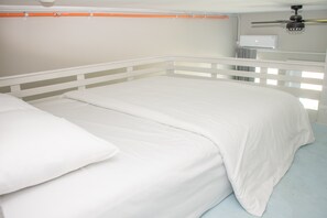 Ein Bett mit weißer Bettwäsche in einem Zimmer, das ein weißes Kopfholz und einen Deckenventilator hat.