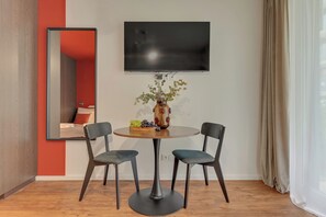 Ein modernes Zimmer mit einem runden Tisch, zwei Stühlen, einer Vase mit Blumen und einem flachbildfernseher an der Wand.