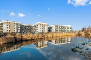 Ein moderner Apartmentkomplex mit mehreren Etagen, einem ruhigen Gewässer im Vordergrund und einem klaren Himmel.