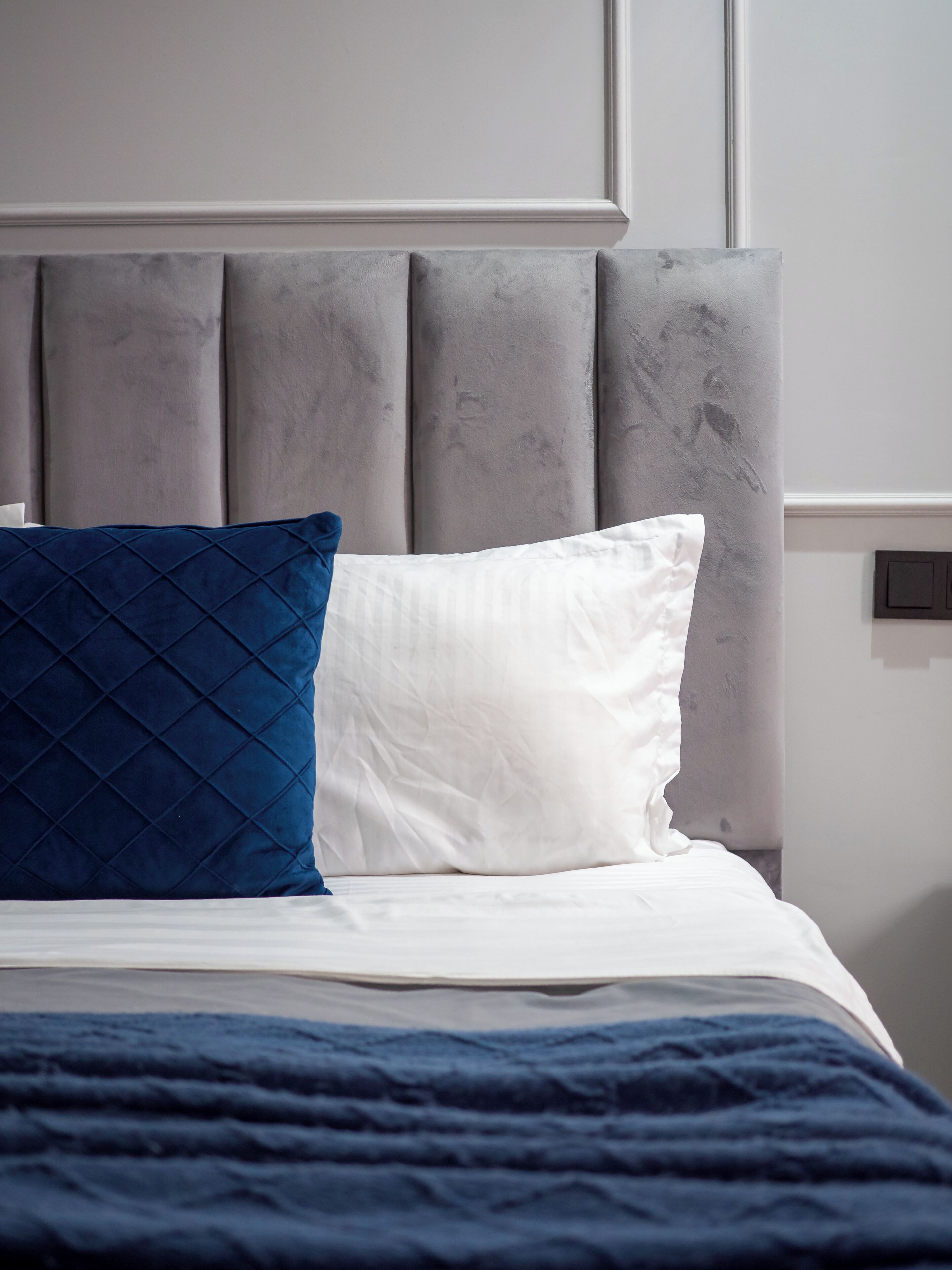 A bed with a grey upholstered headboard, white and blue pillows, and a blue bedspread.