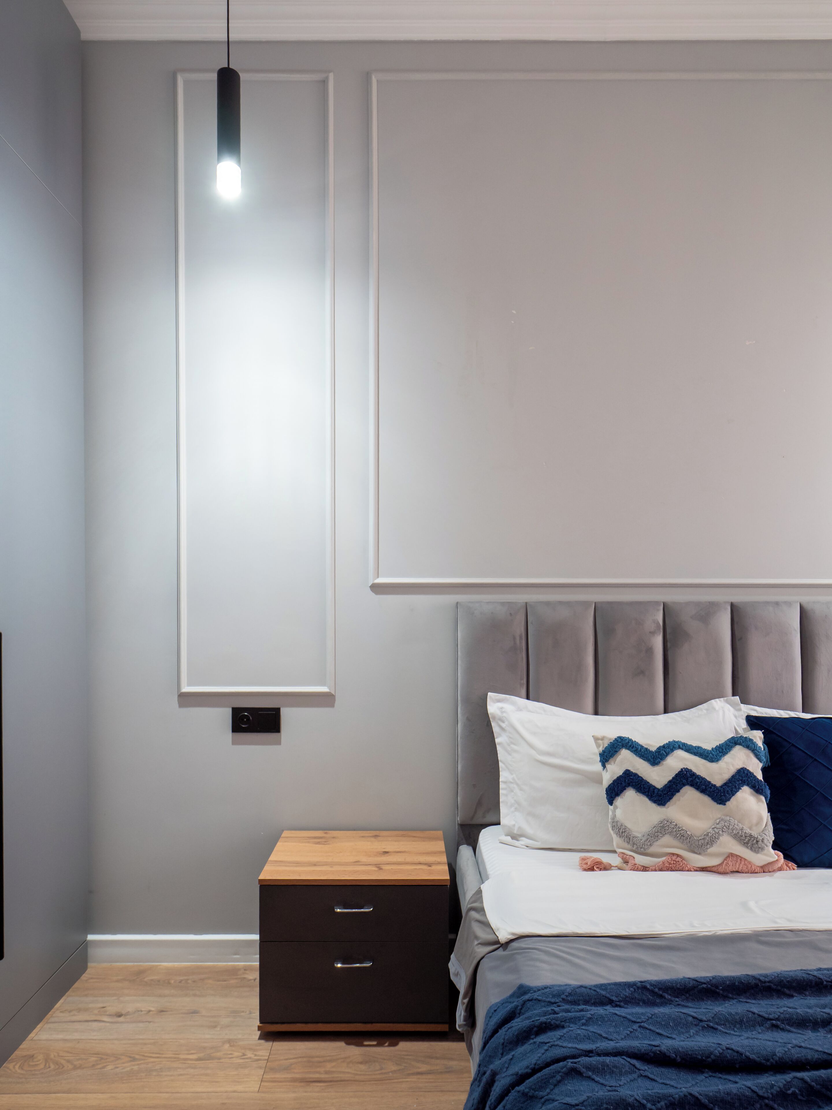 Un dormitorio con cama, mesitas de noche, lámpara colgante y televisor en la pared.