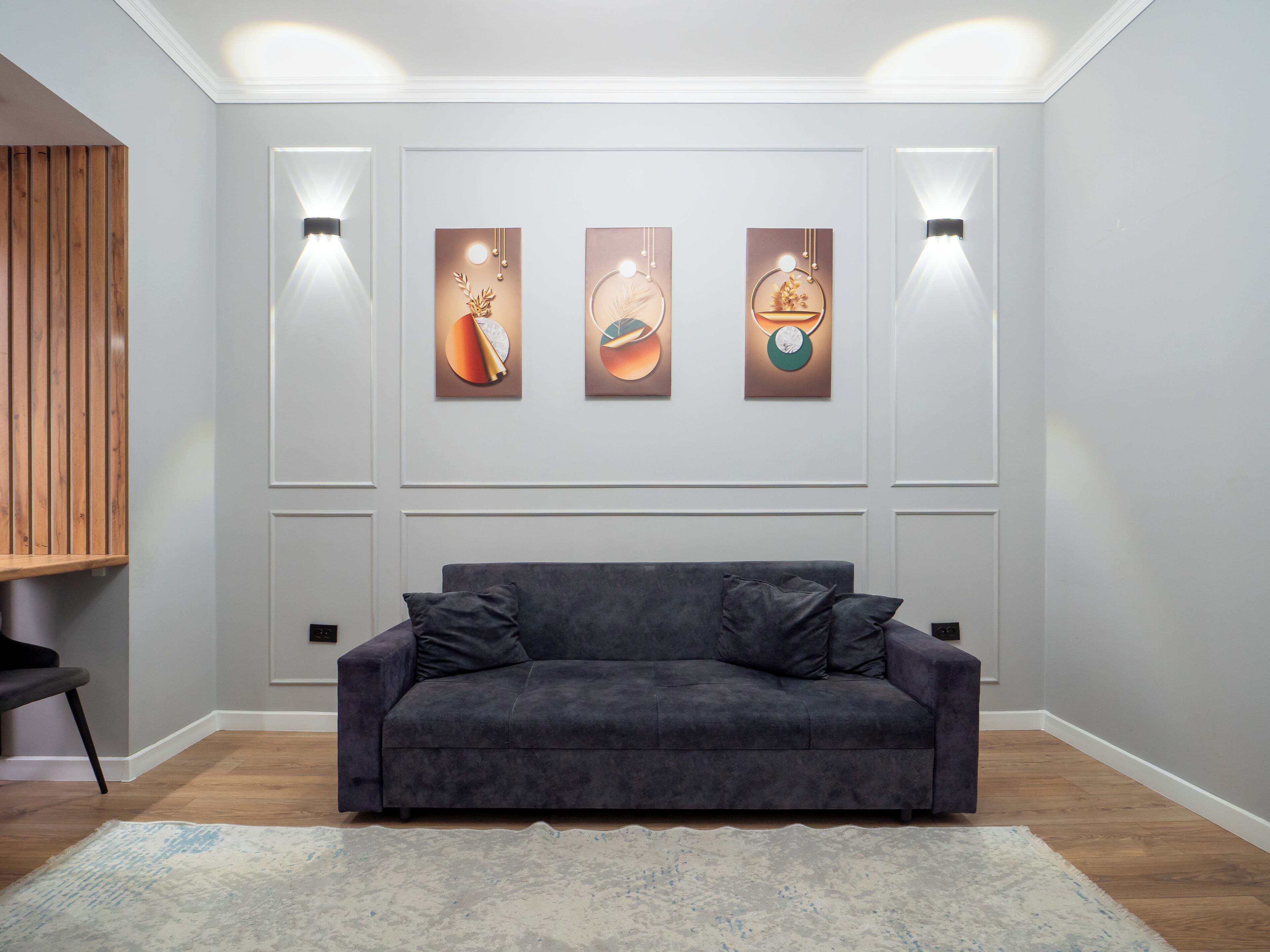 A modern living room with a dark grey sofa, a wooden accent wall, and three wall-mounted light fixtures.