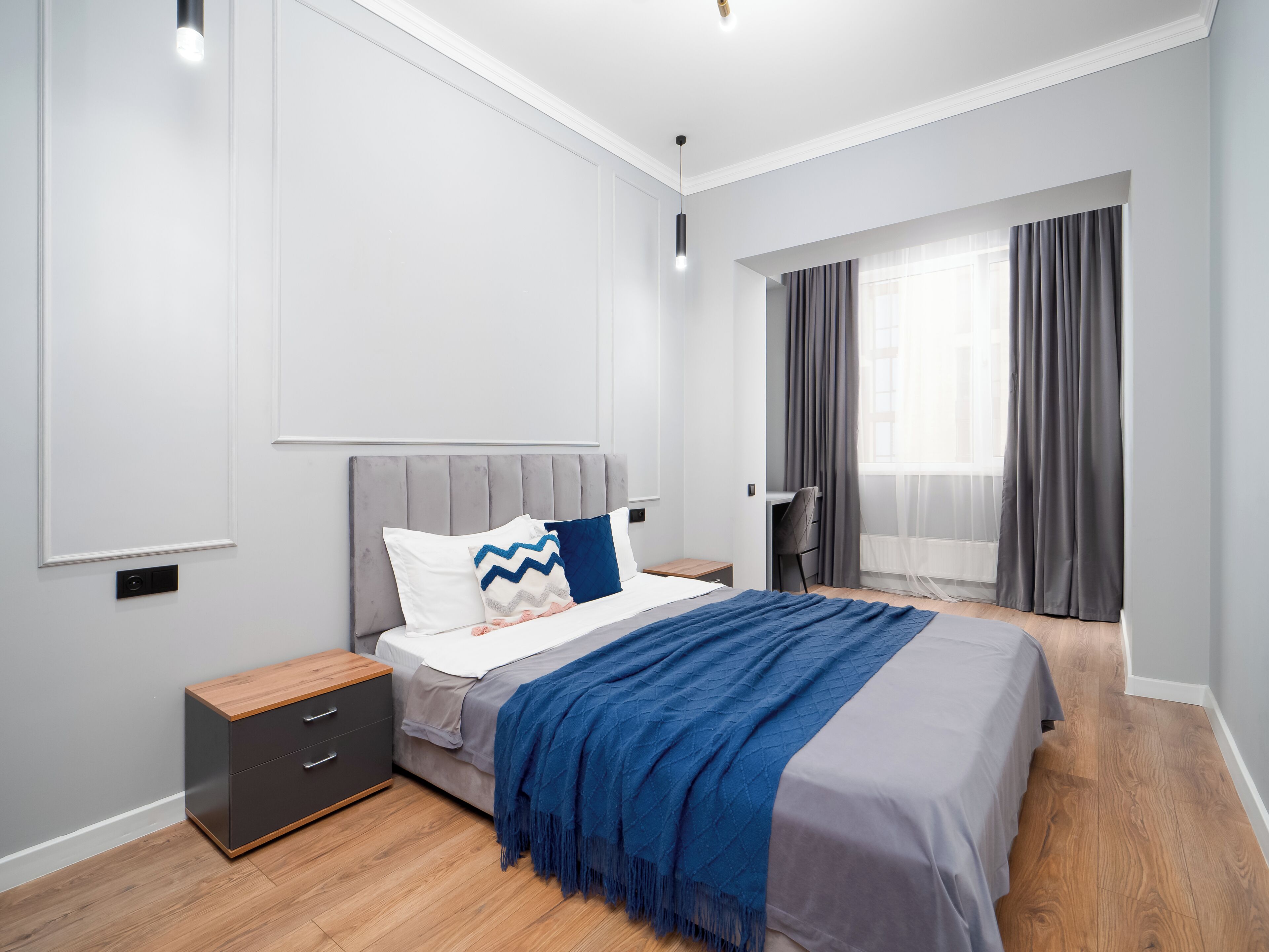 A modern bedroom with a bed, bedside tables, a desk, and a window with curtains.