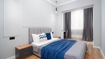 A modern bedroom with a bed, bedside tables, a desk, and a window with curtains.