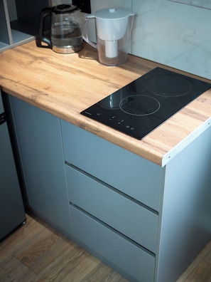 A kitchen with a wooden countertop, a black induction cooktop, and a coffee maker. - Comfort City Residence with beatiful vew (Almaty)