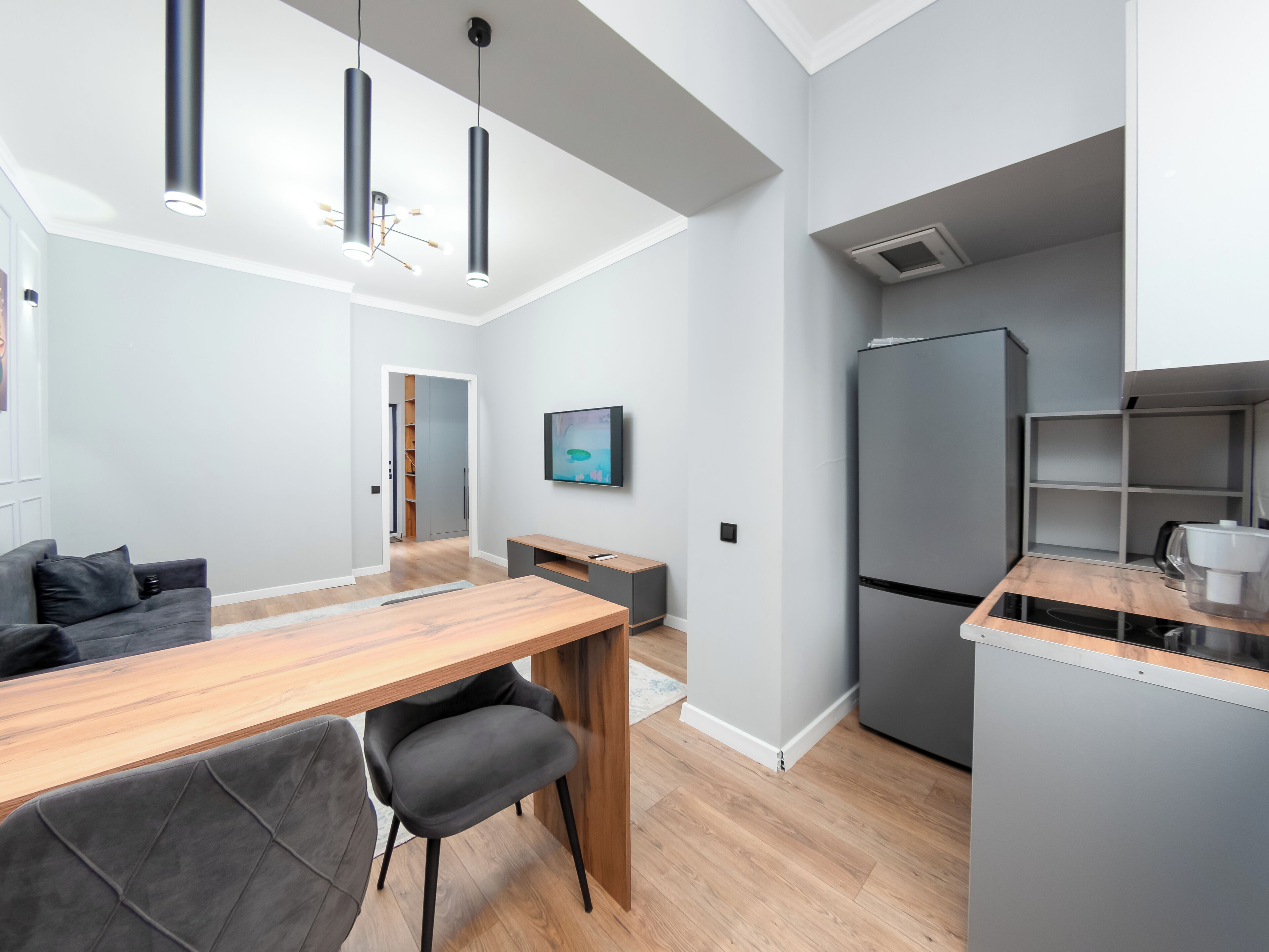 Una cocina moderna con refrigerador integrado, un comedor con mesa y sillas de madera, e iluminación colgante.