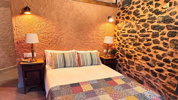 A bedroom with a stone wall, a quilted bedspread, and two bedside lamps.