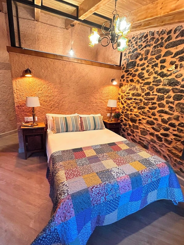 A bedroom with a stone wall, a quilted bedspread, and two bedside lamps.