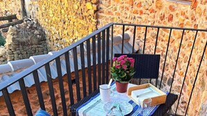 A small outdoor seating area with a table set for two, a chair with a blue throw, and a potted plant.