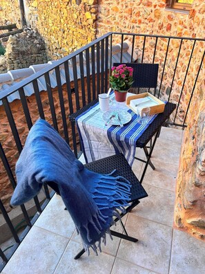 A small outdoor seating area with a table set for two, a chair with a blue throw, and a potted plant.