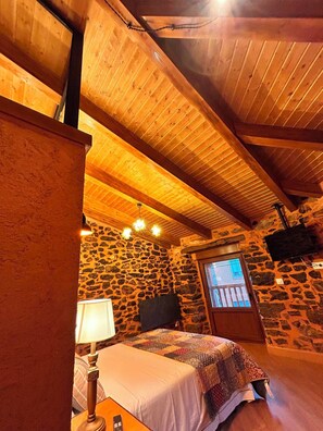 A cozy room with a stone wall, wooden ceiling beams, a bed, a lamp, and a fireplace. - Los Castaños de Morla Cabin near the Teleno Mountains, sleeps 4 (Morla de la Valdería)