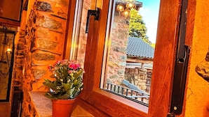 A stone wall with a potted plant on a ledge, a window with a view of a building, and a wooden door.