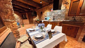 A rustic dining area with stone walls, a wooden table set for two, and a tiled backsplash in the background.
