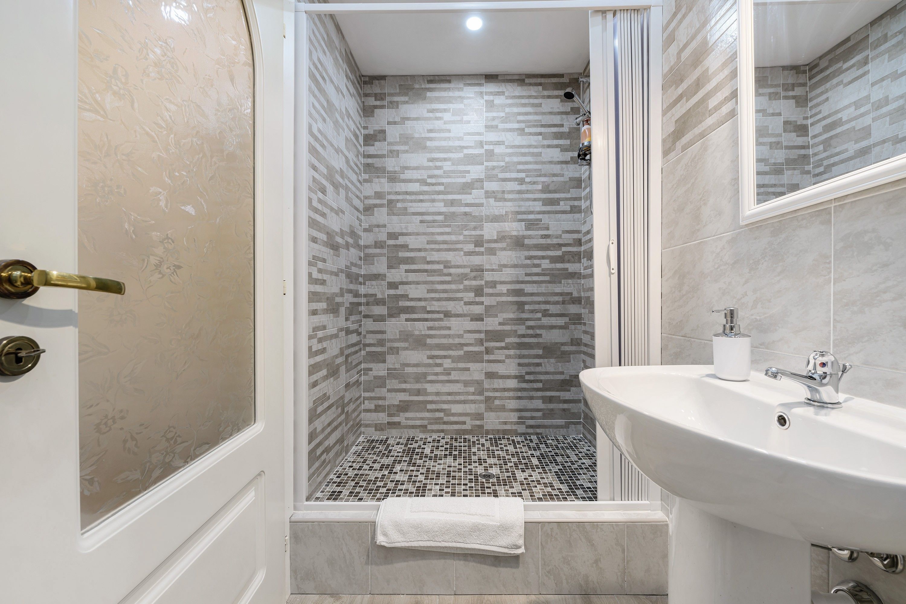 Une salle de bain moderne avec une douche, des murs carrelés, un lavabo et une serviette.