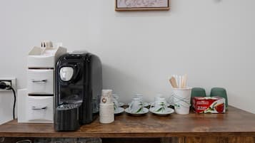 Eine Kaffeestation mit einer Kaffeemaschine, Einwegbechern, einer Schachtel Gold Blush Tee und einem gerahmten Bild an der Wand.