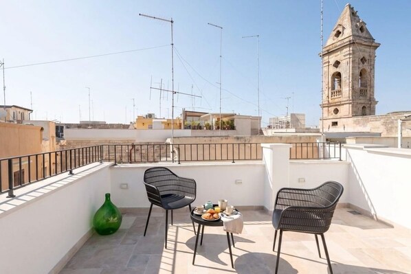 A rooftop terrace with two chairs, a table with breakfast, and a view of a historic tower. - Palazzo Vanese Sus | Boutique Stay with Private Rooftop Terrace (Bari)