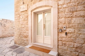 A stone building with a white door, a doormat, and a small window. - Palazzo Vanese Sus | Boutique Stay with Private Rooftop Terrace (Bari)