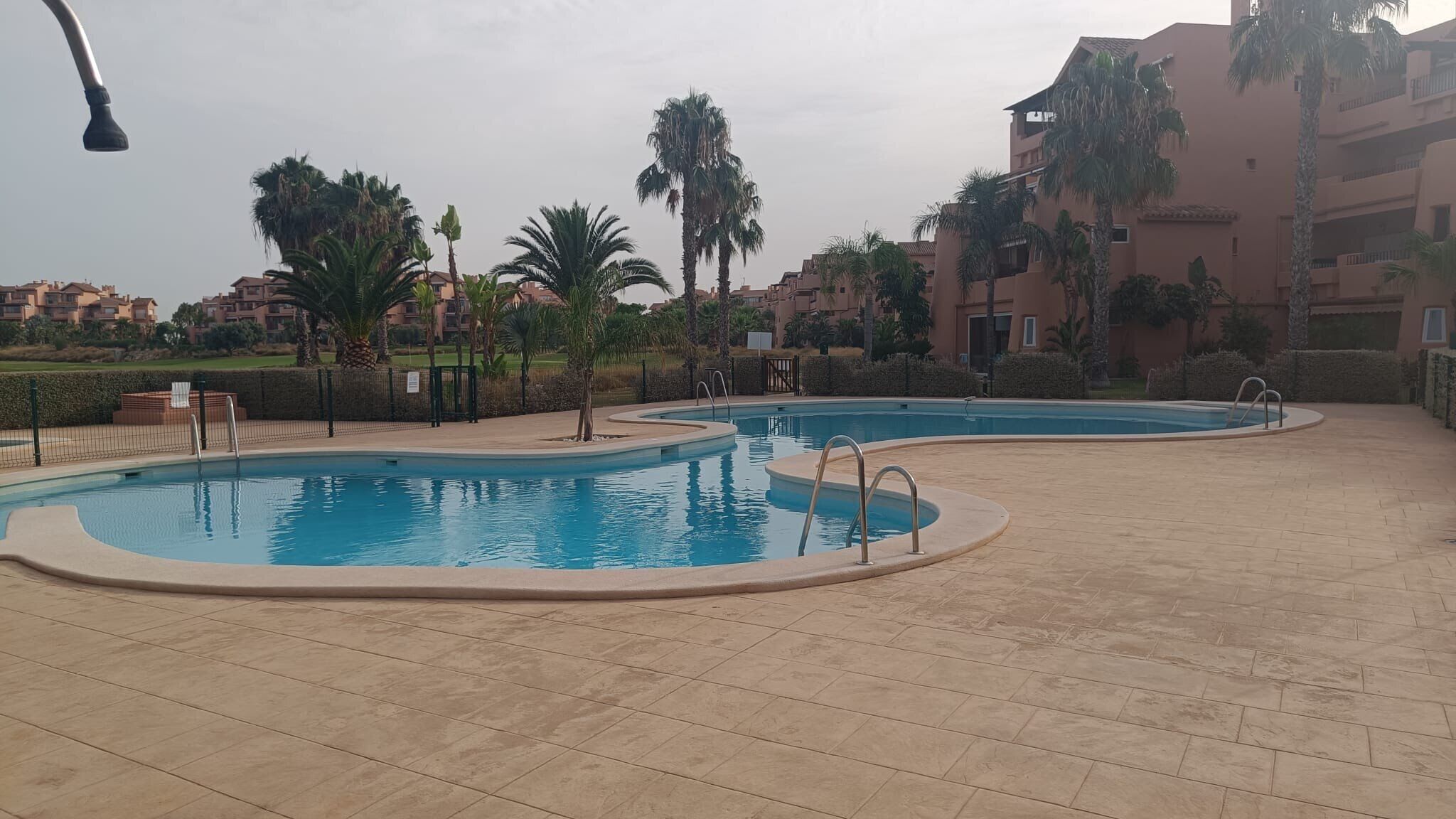 A swimming pool area with two pools, surrounded by palm trees and a building with balconies.