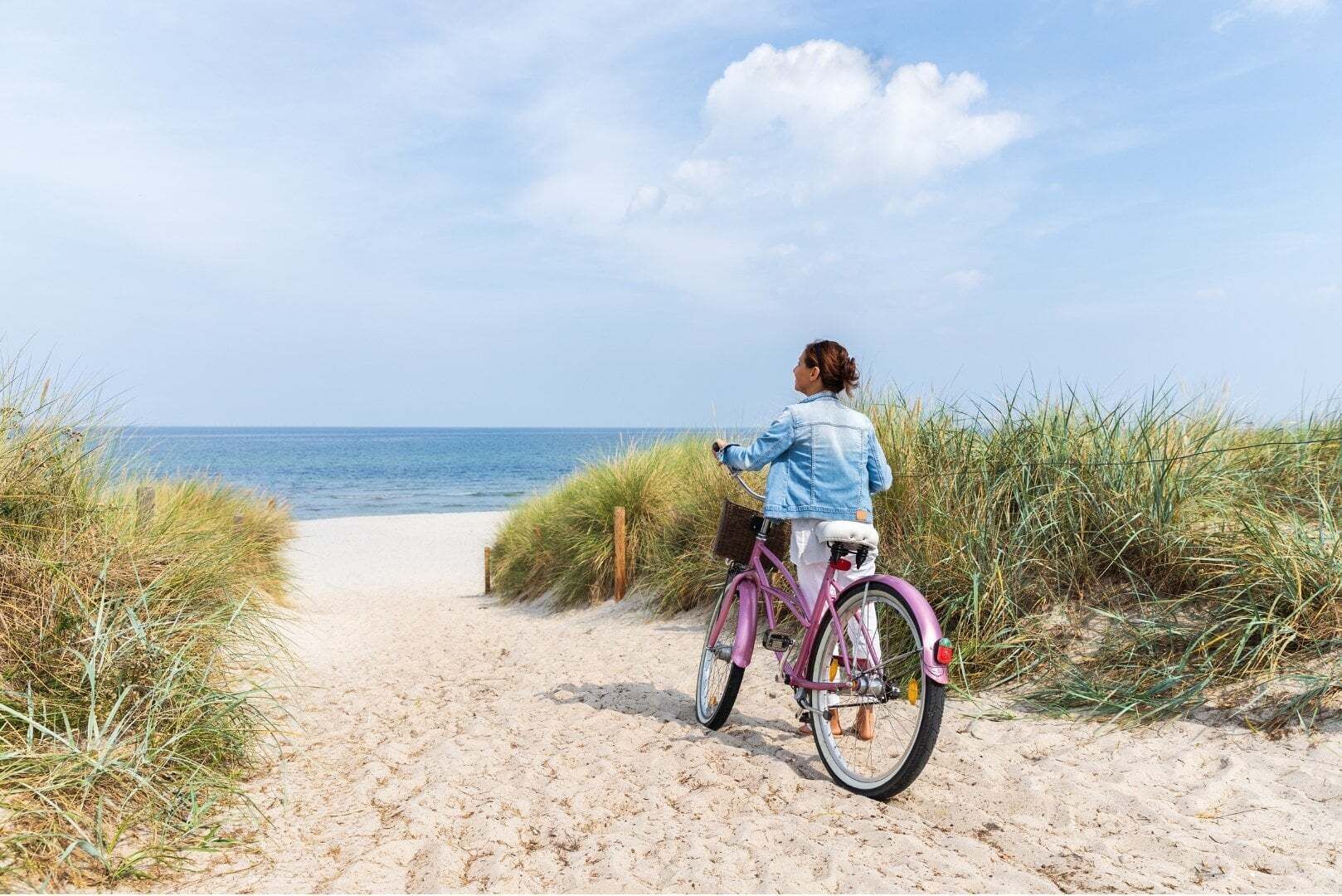 Un sentier sablonneux menant à la plage, sur lequel on aperçoit une personne à vélo.