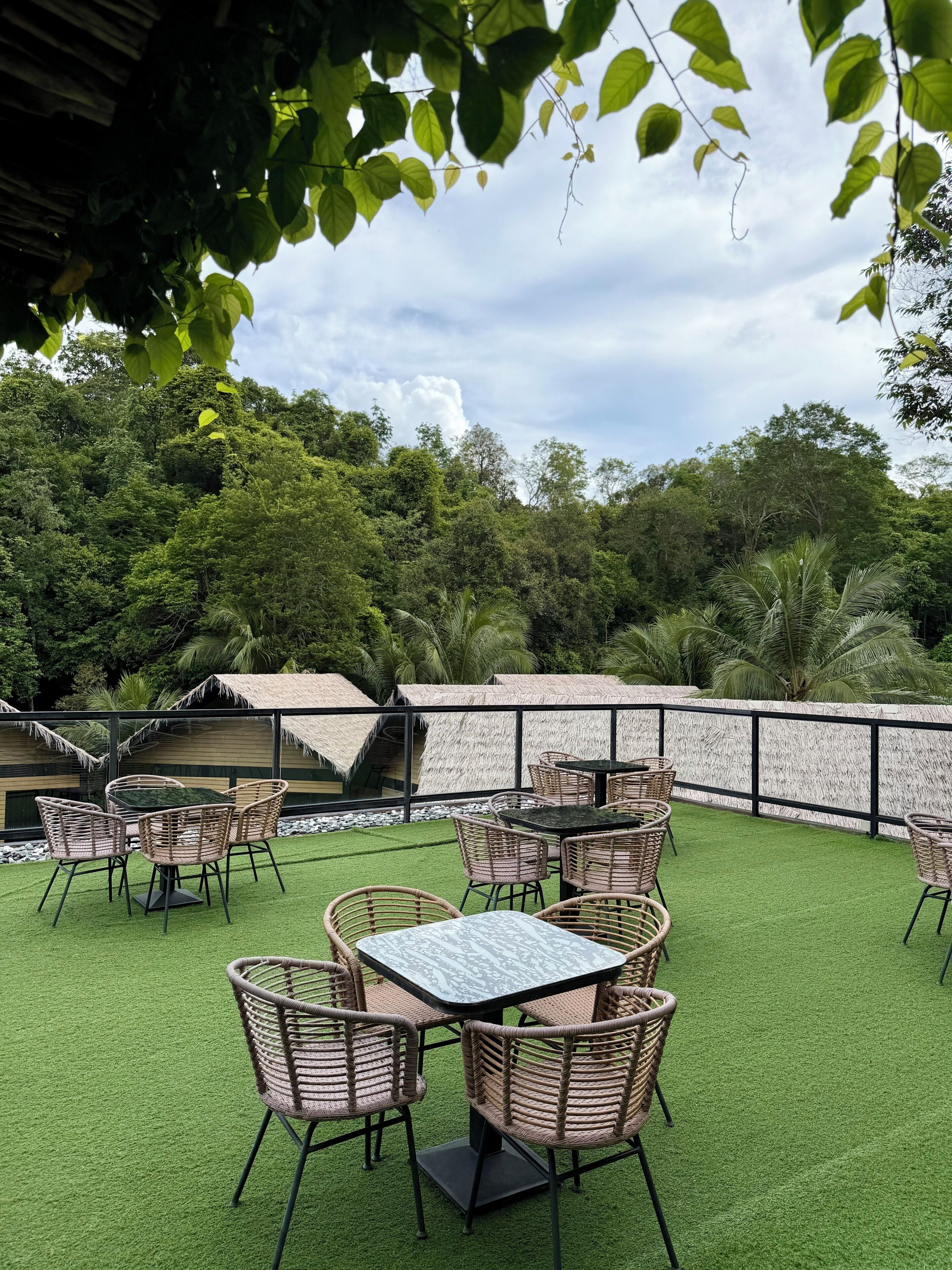 An outdoor seating area with tables and chairs, surrounded by a stone wall and lush greenery.