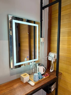 Habitación de hotel con espejo, secador de pelo, teléfono, cafetera y bandeja con artículos de aseo.