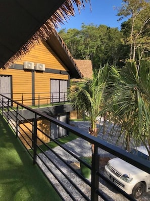 A building with a thatched roof, a balcony with a railing, and a white car parked in front. - A Coral Reefs Resort Langkawi (Langkawi)