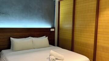 A hotel room with a bed, a wooden headboard, a window with blinds, a wooden wardrobe, and an air conditioning unit.