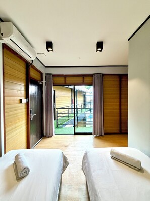 Habitación de hotel con dos camas, una puerta corrediza y vistas a un edificio.