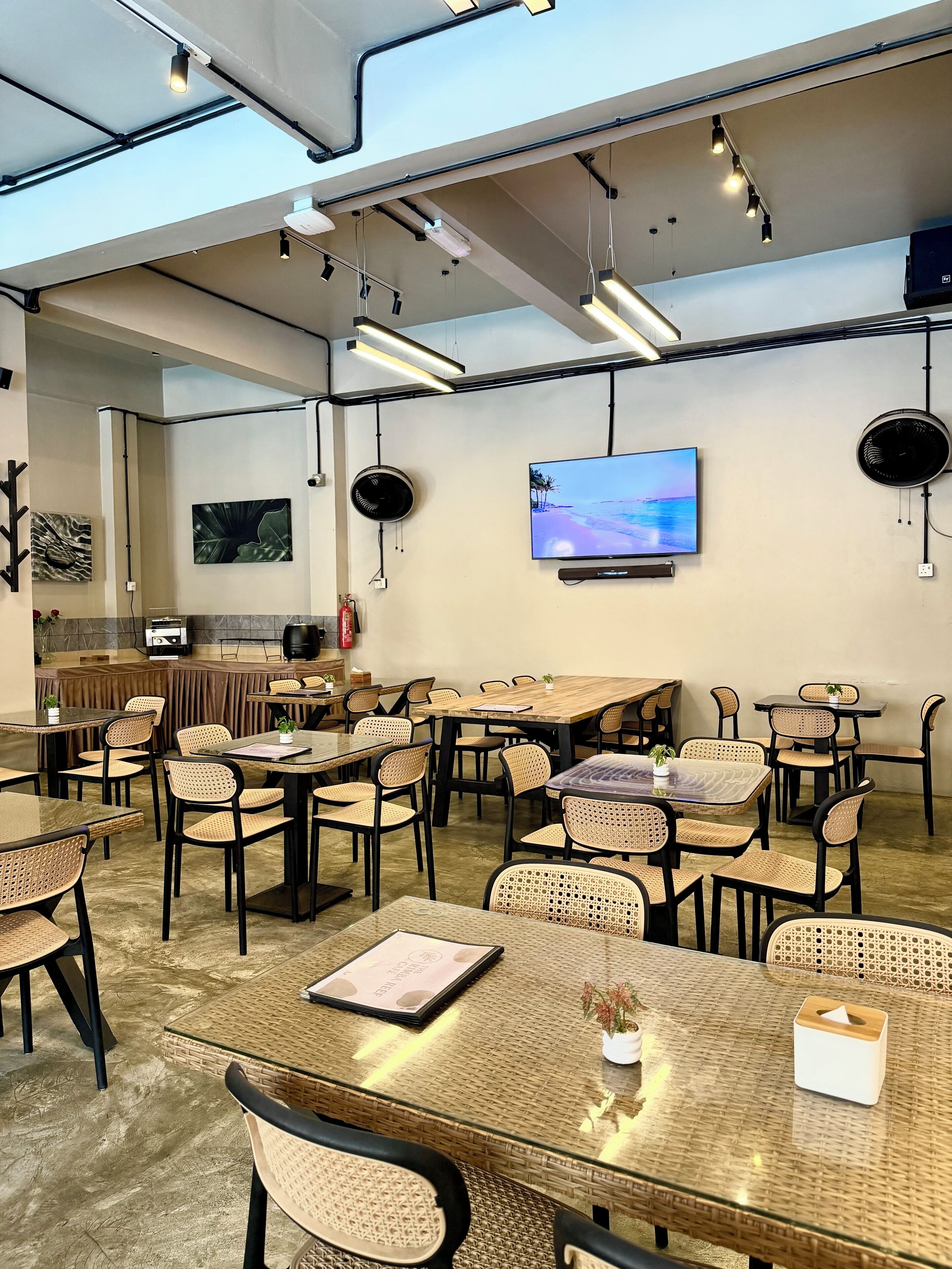 A spacious indoor dining area with multiple tables and chairs, a flat-screen TV mounted on the wall, and ceiling-mounted lighting fixtures.