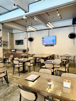Un comedor interior amplio con varias mesas y sillas, un televisor de pantalla plana en la pared y luminarias colgantes.